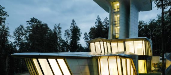 The house is lit from within, shining brightly in contrast to the dark, leafy surroundings.