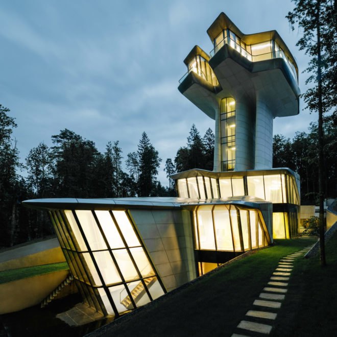 The house is lit from within, shining brightly in contrast to the dark, leafy surroundings.