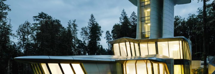 The house is lit from within, shining brightly in contrast to the dark, leafy surroundings.