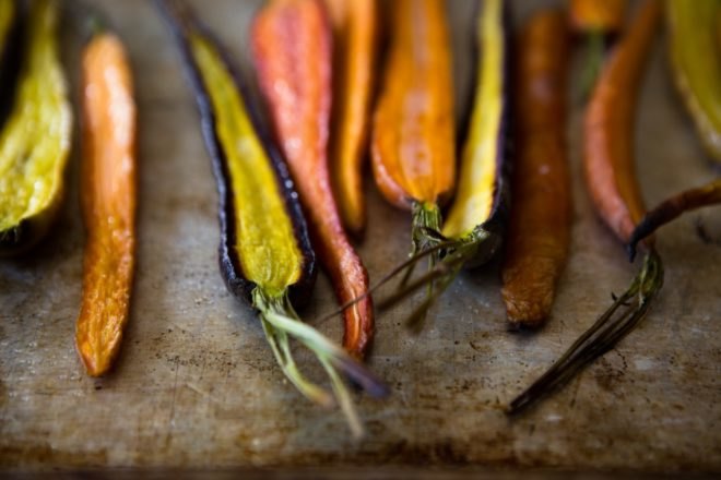 Multicolored roasted carrots rest on a baking tray