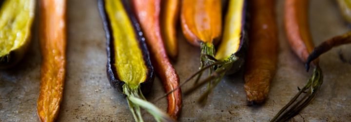 Multicolored roasted carrots rest on a baking tray