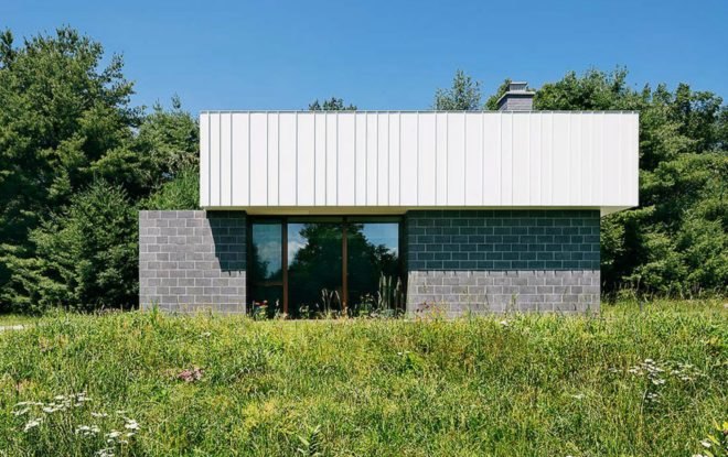 The exterior of the cabin, which has three gray concrete cubic volumes topped with a white metal box for the roof.