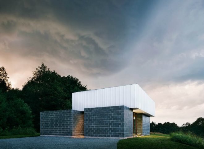 The exterior of the cabin at night. The gray and white angular home is striking against the lush, green surroundings.