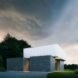 The exterior of the cabin at night. The gray and white angular home is striking against the lush, green surroundings.