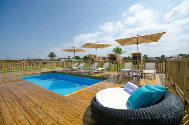 Behind the bungalows is a shared pool area, with umbrella-covered tables and lounge chairs.