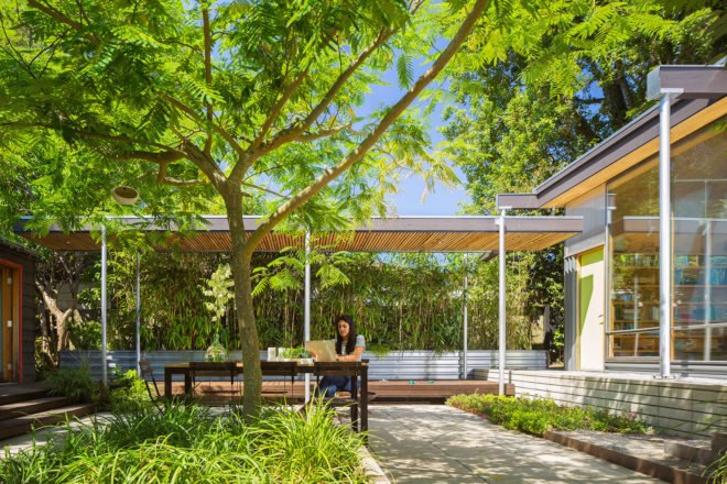 A woman sits at a table in a greenery-filled courtyard.