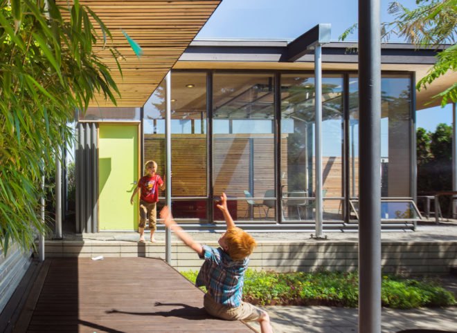 Two children play outside the house, which features large glass windows.
