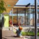 Two children play outside the house, which features large glass windows.
