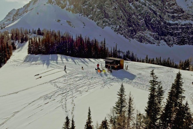 An aerial photo of the Honomobar on the snow-covered mountain. Several snowboarders sit in chairs in front of the bar.