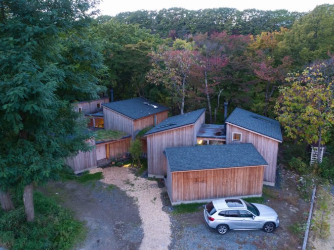 An aerial view of several wooden cabins with a silver SUV in front.