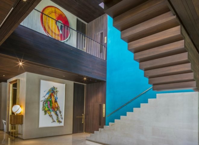 Against the interior stairs is a bright blue wall. This room is filled with art hanging on the walls.