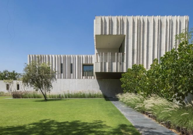 The monolithic stone home contrasts with the luscious green gardens.