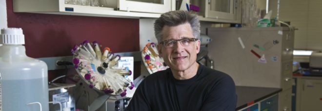 Jeff Brinker, a scientist, sits on a stool in a lab.