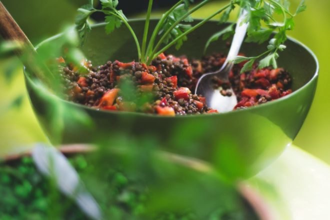 A healthy vegetarian lentil salad with a spoon in a green bowl