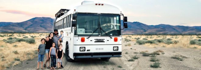 Gabriel and Debbie Mayes stand with their four children outside a white bus. They converted this bus into a tiny home.