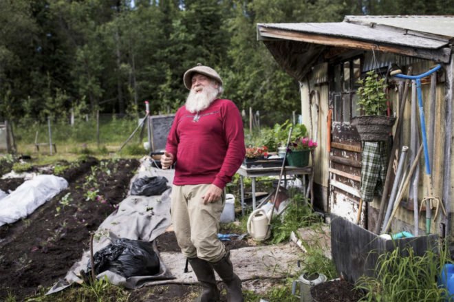 A citizen of McCarthy Alaska stands in front of his rustic home