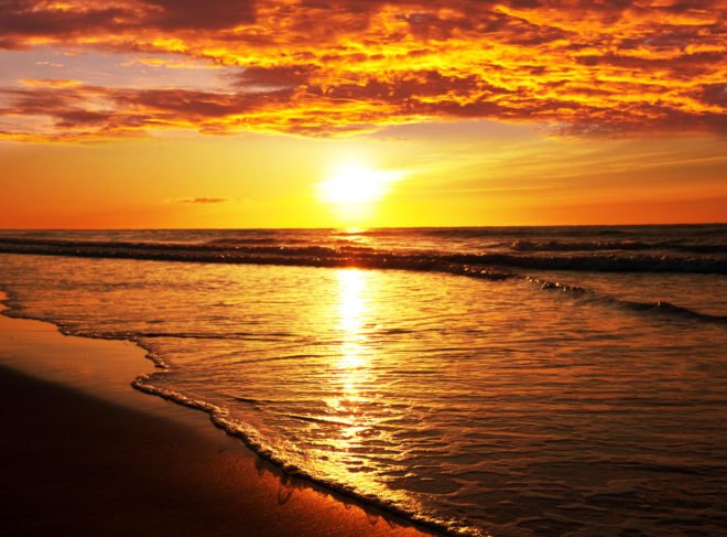 A bright red, orange and yellow sunset against the ocean.