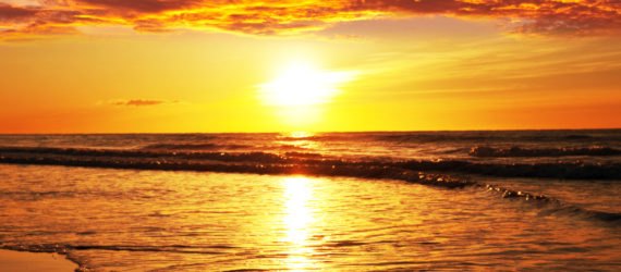 A bright red, orange and yellow sunset against the ocean.