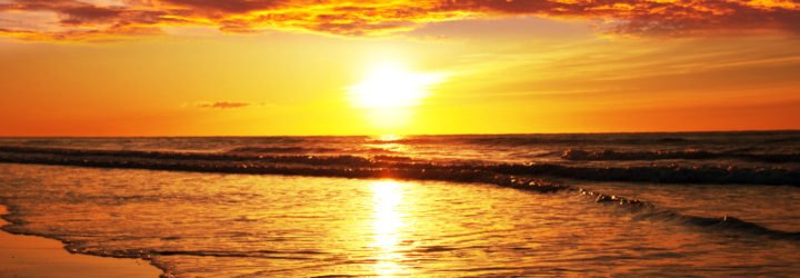 A bright red, orange and yellow sunset against the ocean.