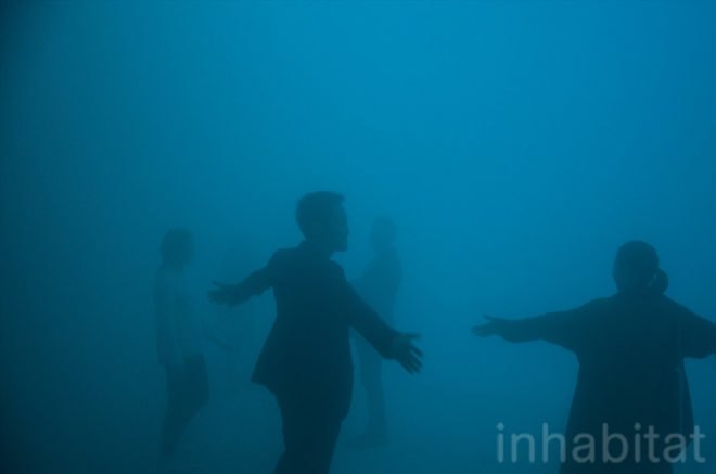 People stand inside the mist-filled dome with their arms stretched out.