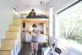 Samantha Garlow holds her baby in the middle of a tiny home. Her husband looks down at them lovingly from the lofted bed.