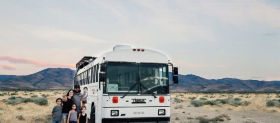 Gabriel and Debbie Mayes stand with their four children outside a white bus. They converted this bus into a tiny home.