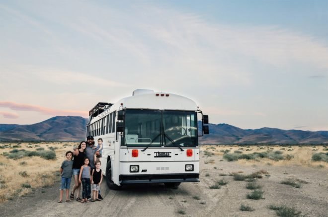 Gabriel and Debbie Mayes stand with their four children outside a white bus. They converted this bus into a tiny home.