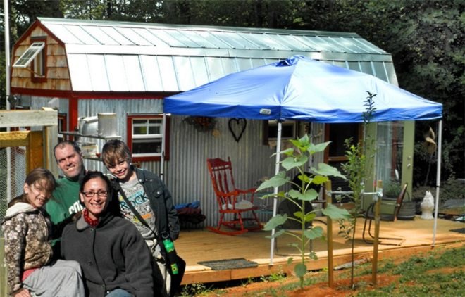 Karl and Hari Berzins and their two children stand outside the tiny home they built using salvaged materials.