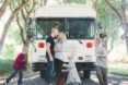 Brandon and Ashley Trebitowski look at each other while their three children run around them. The family is in front of a white bus that they converted into their tiny home.