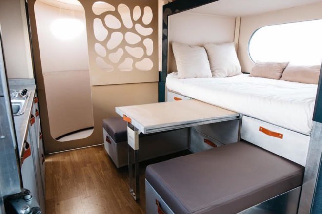 A bed, table, and chairs inside the travel pod.