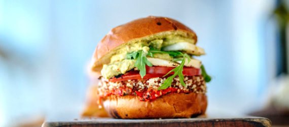 A burger made of greens and vegetables resting on a cutting board