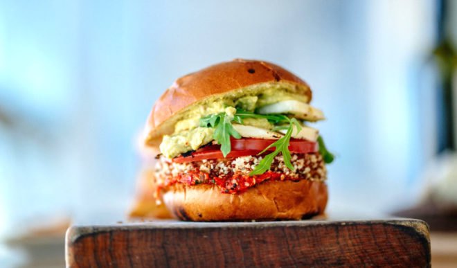 A burger made of greens and vegetables resting on a cutting board