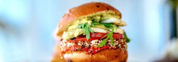 A burger made of greens and vegetables resting on a cutting board