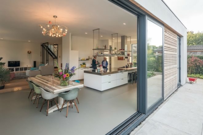 Two people chat in the kitchen space. Just beyond the dining table is the couch and television in the living area.