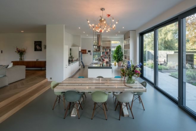 The dining area features a sleek wooden table with green and blue chairs and a chandelier above the table.