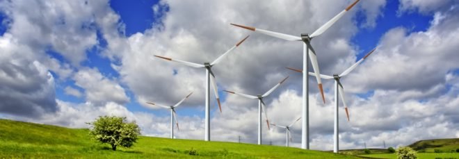 Wind turbines are on rolling green hills.