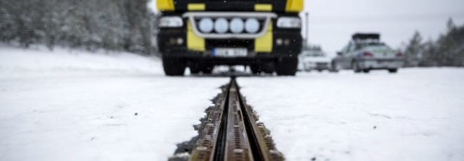 An electric truck drives down a snow-covered electrified road that charges the vehicle as it drives.