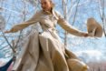 Model twirls in a tan trench coat and holds a tan hat, both items made from recycled water bottles.