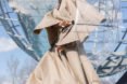 Model in a tan trench coat holds a clear umbrella.