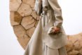 Model wears trench coat and holds a hat.