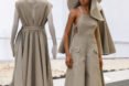 Model stands next to a mannequin. The model is wearing a large floppy hat and a wide leg jumpsuit.