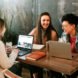 Three people are sitting at a table, hunkered over their laptops and laughing.