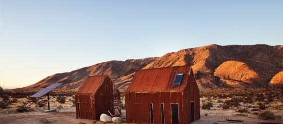 pair of rusted steel clad cabins in the desert