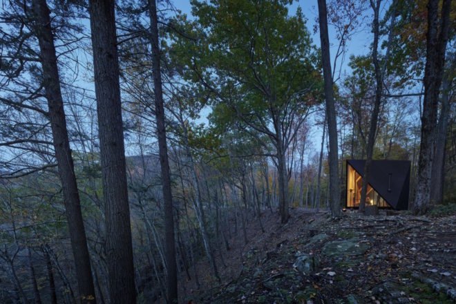 A triangular tiny house in a forest at night