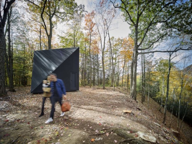 Two people walking in front of a triangular tiny house