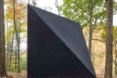 A black, triangular tiny house in the woods