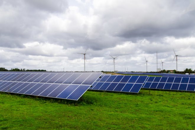 Solar panels in a green field with wind turbines in the background