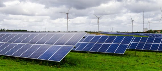 Solar panels in a green field with wind turbines in the background
