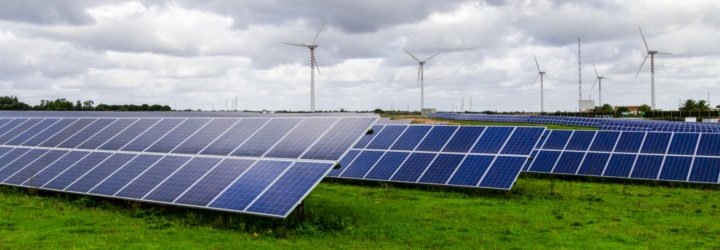 Solar panels in a green field with wind turbines in the background