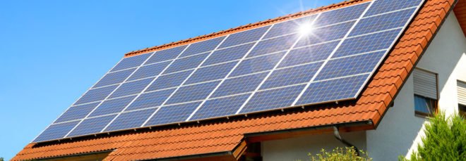 Solar panel on a red roof reflecting the sun and the cloudless blue sky